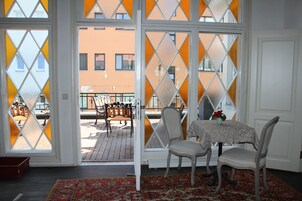 A room with a large window, a dining table with chairs, and a view of the street outside.