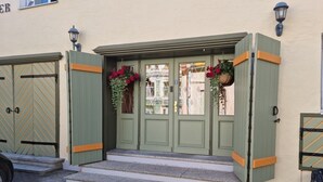 Ein Gebäude mit grüner Fassade, doppelte Türen mit orangefarbenen Akzenten und einige Stufen, die zum Eingang führen.