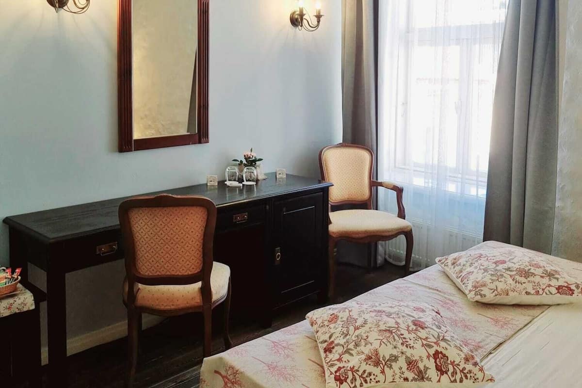 Une chambre d’hôtel comprenant un lit, deux chaises, un bureau, une commode, un miroir et deux appliques murales.