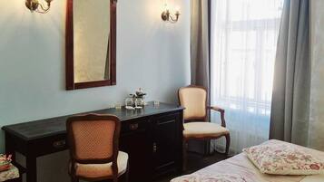 Habitació d'hotel amb un llit, dues cadires, escriptori, tauleig i un mirall, juntament amb dues parets amb llums.