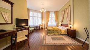 Ein Hotelzimmer mit Holzboden, einem Bett mit floralem Überwurf, einem Schreibtisch mit Fernseher, einem Sessel und einem Nachttisch mit Lampe.