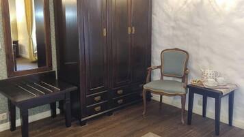 Una habitación con un armario de madera oscura, una silla, una mesita con tetera y una alfombra estampada.