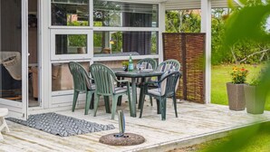 Een terras buiten met een tafel en stoelen, een schuifpui en uitzicht op de tuin.