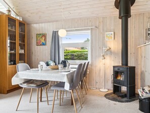 Un coin repas chaleureux avec une table dressée pour quatre personnes, un buffet en bois doté de portes en verre et un poêle à bois noir.