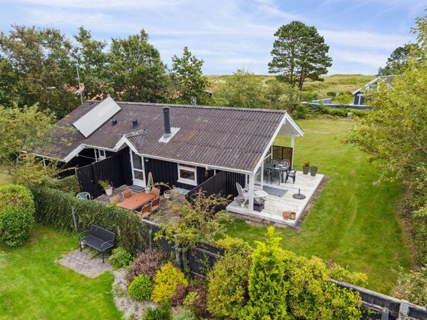 Une maison à deux étages avec un toit en pente, une terrasse couverte et une cour arrière clôturée.