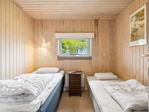 Une petite chambre accueillante avec deux lits, une fenêtre donnant sur les arbres et une petite table avec un livre.