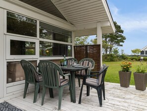 Une terrasse couverte avec une table et des chaises, de grandes fenêtres et une vue sur un jardin.