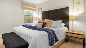 Een slaapkamer met een bed, nachtkastjes, een bankje en kunstwerken aan de wanden.