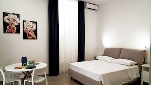 Un dormitorio con cama, mesita de noche, silla y dos cuadros en la pared.