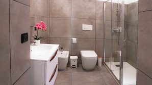 Un baño moderno con cabina de ducha de vidrio, un lavabo blanco y un inodoro.