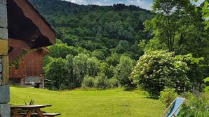 A wooden cabin with a stone foundation, a grassy yard, a picnic table, and a blue lawn chair.