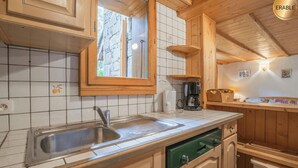 A kitchen with wooden cabinets, a stainless steel sink, a coffee maker, and a window with a view of trees.