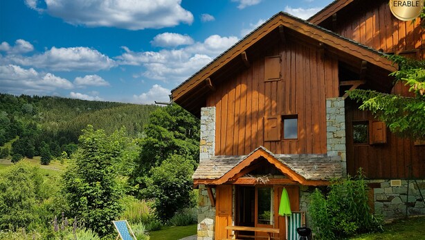 A wooden cabin with a stone foundation, a porch, and a green umbrella.
