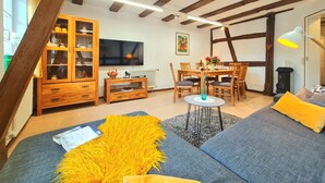 Ein gemütliches Wohnzimmer mit freiliegenden Holzbalken, einem Essbereich mit Tisch und Stühlen sowie einem Sofa mit gelber Decke.
