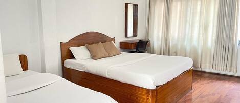 Una habitación de hotel con dos camas, suelo de madera, un escritorio con una silla, un espejo y una ventana con cortinas.