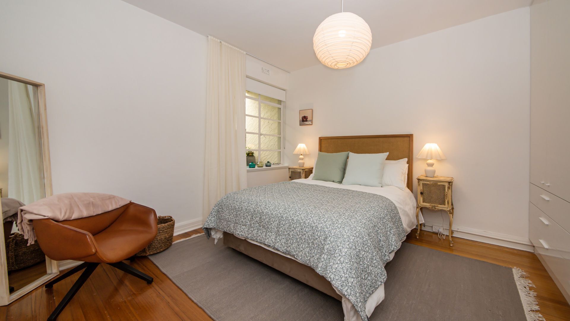 Une chambre à coucher comprenant un lit, une chaise, une table de chevet, une lampe, une fenêtre et un luminaire suspendu.
