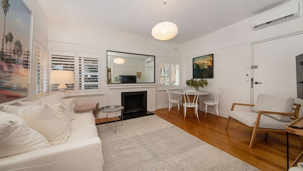 A modern living room with a white sofa, a fireplace, a dining area with white chairs, and a large mirror. - Pet Friendly - Charnwood Charm in St Kilda (St Kilda)