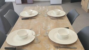 A dining table set with white plates, bowls, and cutlery, surrounded by chairs. - Peaceful cottage with spa and air conditioning in Couzon (Couzon)