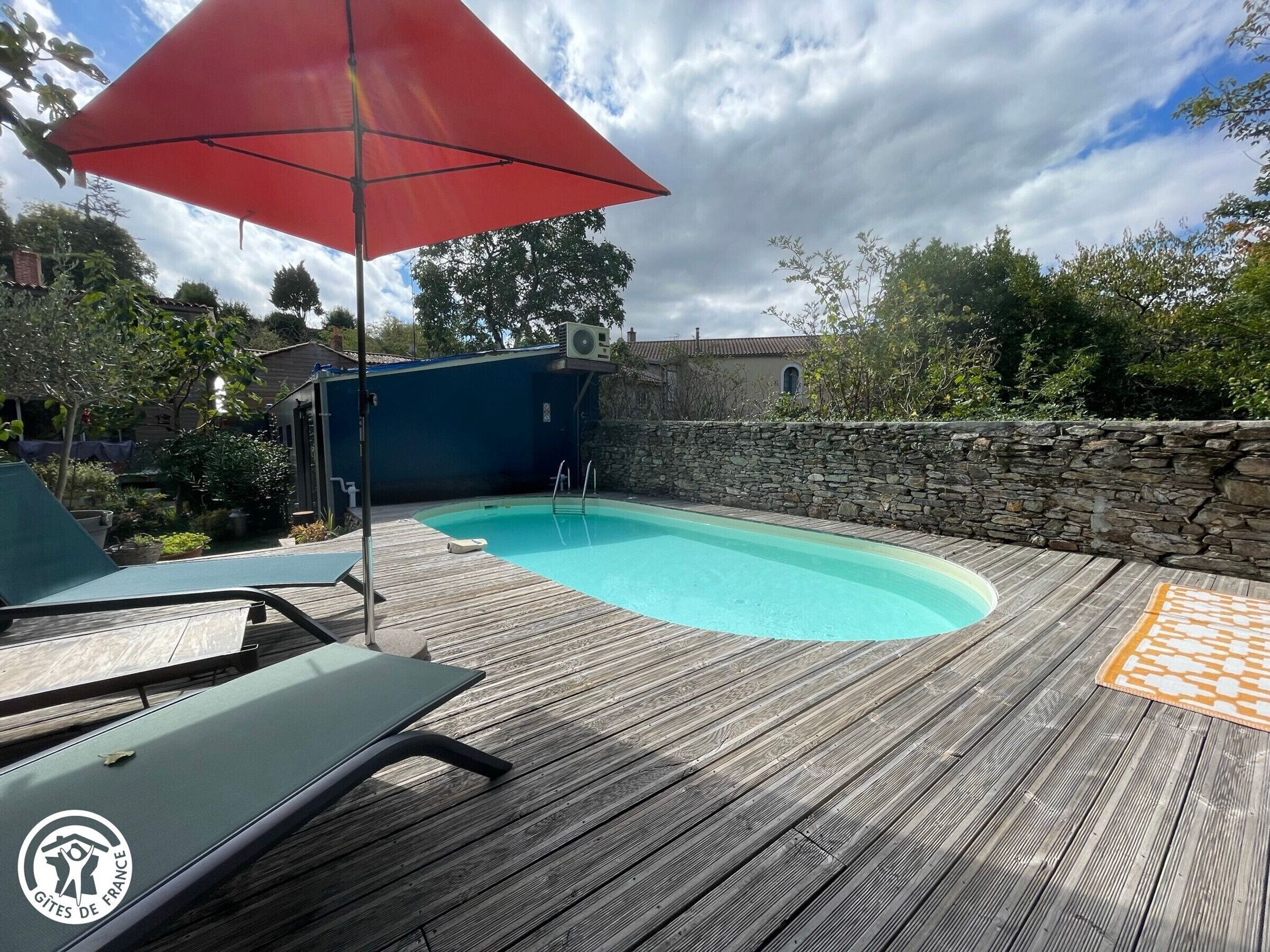 A wooden deck with a swimming pool, lounge chairs, and a stone wall.