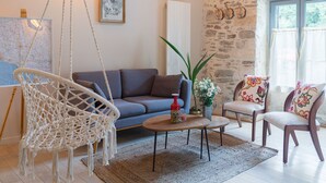 A cozy living room with a macrame chair, a sofa, and a coffee table. There is a stone wall and a window with curtains. - Renovated House with Shared Pool and Garden in Mareuil-sur-Lay, Sleeps 6 (Mareuil-sur-Lay-Dissais)
