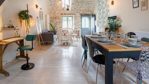 A dining area with a wooden table set for four, surrounded by chairs, a hanging chair, and a stone wall in the background. - Renovated House with Shared Pool and Garden in Mareuil-sur-Lay, Sleeps 6 (Mareuil-sur-Lay-Dissais)
