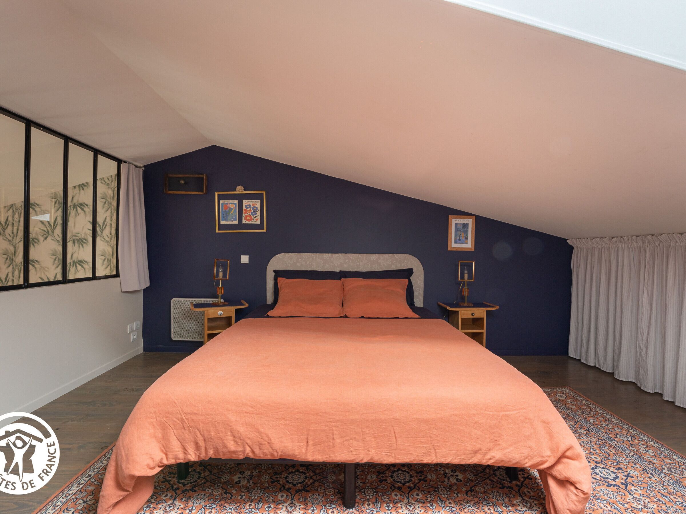 A bedroom with a large bed, two bedside tables, a window with curtains, and a patterned rug.