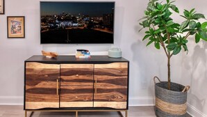 Ein modernes Wohnzimmer mit einem Holzkabinett, einem Flachbildfernseher und einer Topfpflanze.