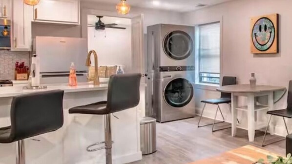 Una cocina moderna con una isla central, un comedor con mesa y sillas, y un mueble grande para electrodomésticos.