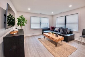 Una sala de estar moderna con una mesa de centro de madera oscura, un sofá negro con cojines, una silla negra y un espejo grande en la pared.