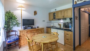 A compact kitchen with wooden cabinets, a dining table with chairs, a television, and a large plant. - Cozy 1-Bed Apartment for 4 with Garden, Parking, Near Cauterets Center and Thermal Spa (Cauterets)