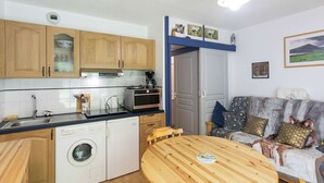 A compact kitchen with wooden cabinets, a dishwasher, a coffee maker, and a dining table. - Cozy 1-Bed Apartment for 4 with Garden, Parking, Near Cauterets Center and Thermal Spa (Cauterets)