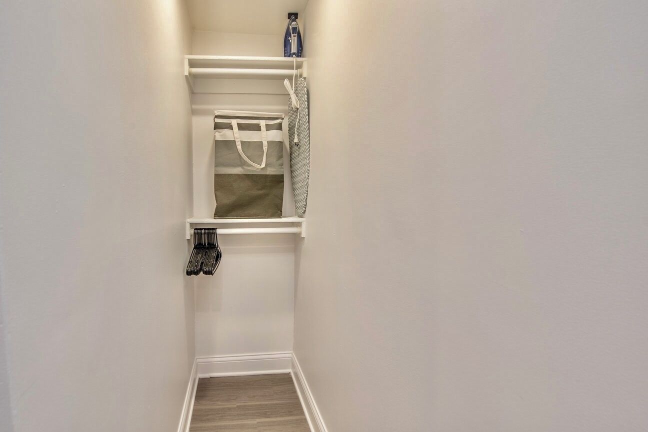 Un pasillo estrecho con una zona de baño pequeña. Incluye un estante con una toalla, una bolsa colgada y un cortinón de ducha.