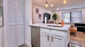 Una cocina moderna con armarios blancos, lavavajillas de acero inoxidable, un fregadero y luces colgantes.