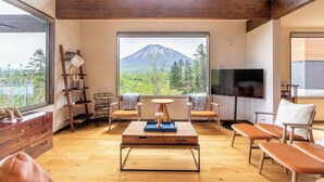 Una sala de estar moderna con suelo de madera, un ventanal con vista a la montaña, un televisor y una mesa de centro.
