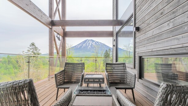 Una terraza de madera con mobiliario de mimbre y una mesa de vidrio, con vistas a la montaña.