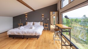 Un dormitorio moderno con una cama grande, suelo de madera y vistas a un paisaje montañoso a través de un ventanal amplio.