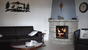 A living room with a stone fireplace, a black leather sofa, a round coffee table, and a wall clock.