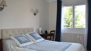 A bedroom with a large bed, a nightstand, a chair, a table, and a window with curtains.