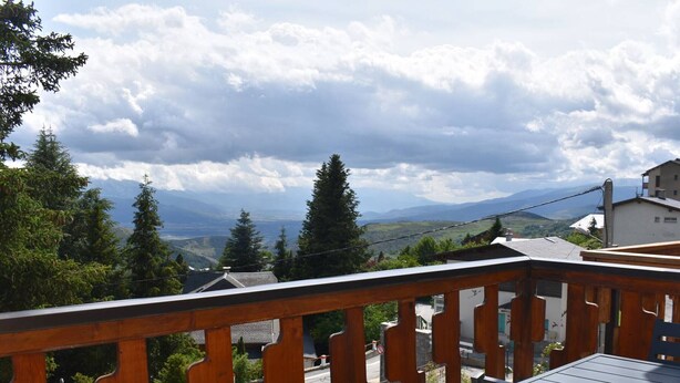 A balcony with a wooden railing overlooking a road and distant mountains.