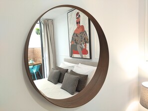 Un dormitorio con cama, almohadas, un espejo grande y un cuadro en la pared.