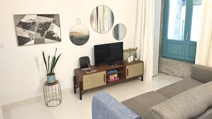 En stue med sofa, fjernsyn på et træstel, verdenskort-kunstværk og et vindue med gardiner.