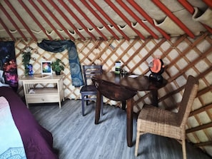 A cozy room with a wooden desk, two chairs, a bed, and a wall-mounted heater.