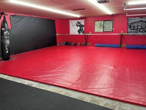 A red padded training area with a punching bag, mats, and a black banner with motivational words.
