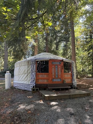 A stationary, single-story, tent-like structure with a patterned door and a small porch area, surrounded by trees.