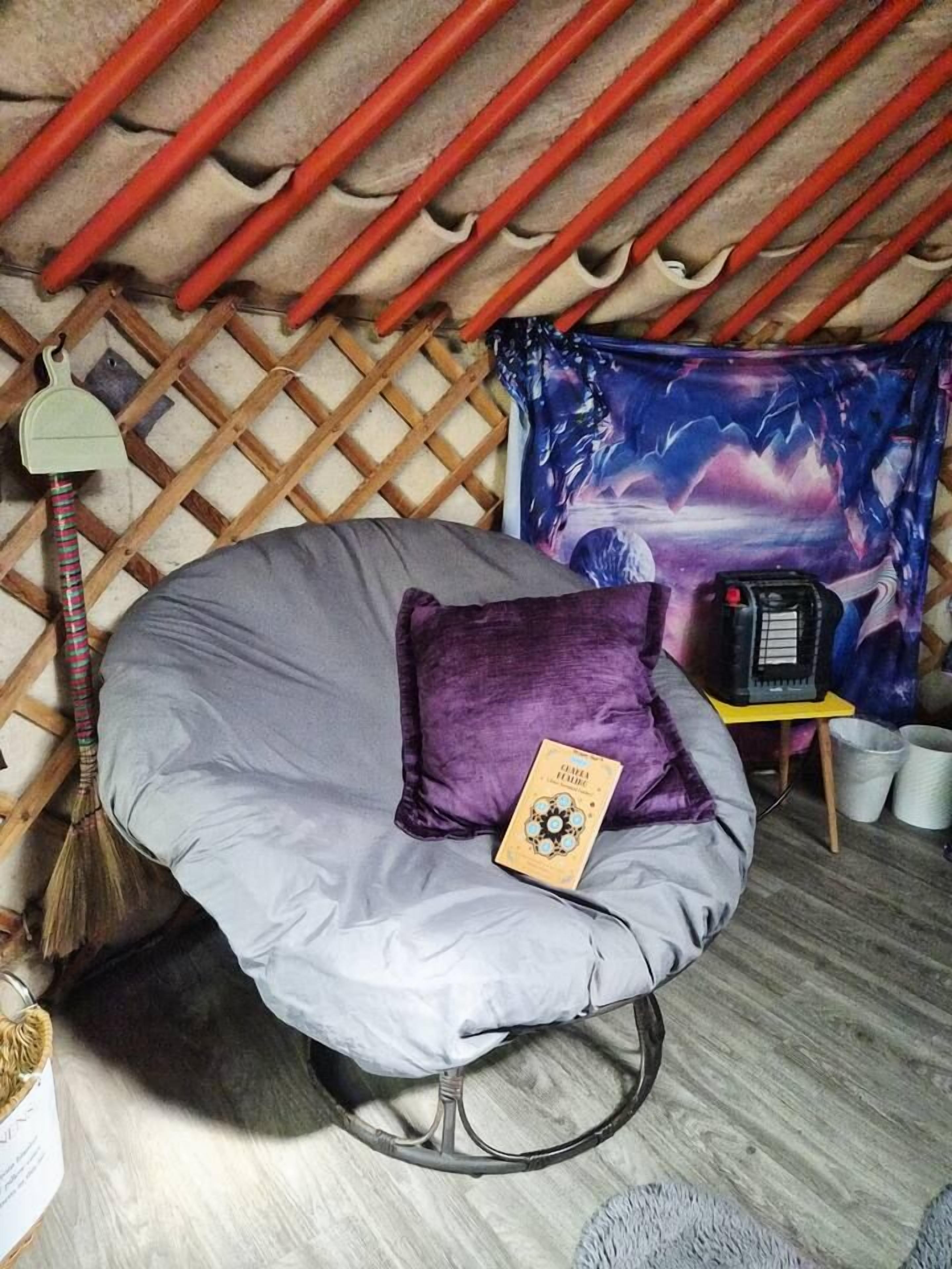 Ein Zimmer mit geneigter Decke, einem einzelnen Sitzsack, einem kleinen Tisch mit einem Radio und einer gemusterten Wandteppich.