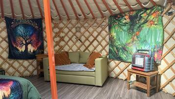 A cozy interior of a yurt with a sofa, a heater, and two tapestries.