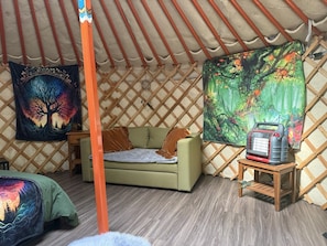 A cozy interior of a yurt with a sofa, a heater, and two tapestries.