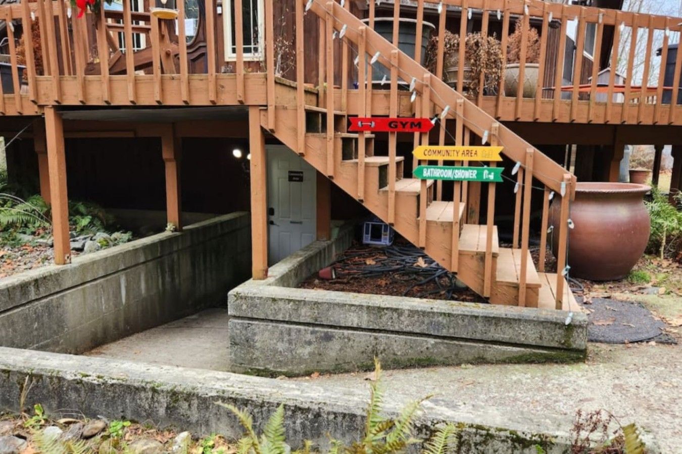 Un escalier en bois mène à une terrasse où un panneau indique l’emplacement d’une salle de sport et d’un espace communautaire.
