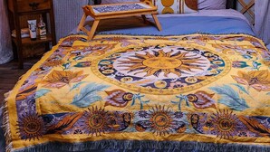 A bed with a colorful, patterned bedspread, a wooden headboard, and a bedside table with a lamp.