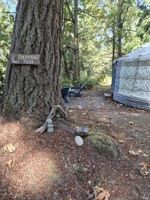 A campsite with a large tree, a sign reading 'Celestial Yurt,' and a covered structure.